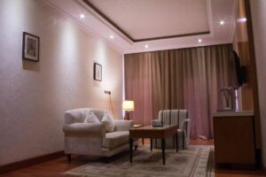 Cozy living area featuring a white couch, striped armchair, coffee table, warm lighting, and elegant curtains.