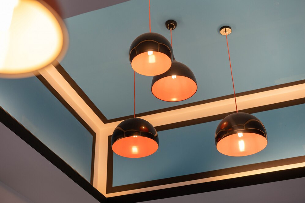 Modern ceiling with three black pendant lights, featuring orange interiors, set against a blue backdrop with geometric trim.