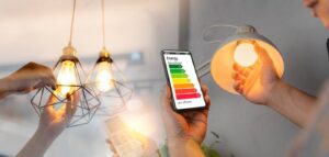Hands handling light fixtures while a smartphone displays an energy efficiency rating for lighting options.
