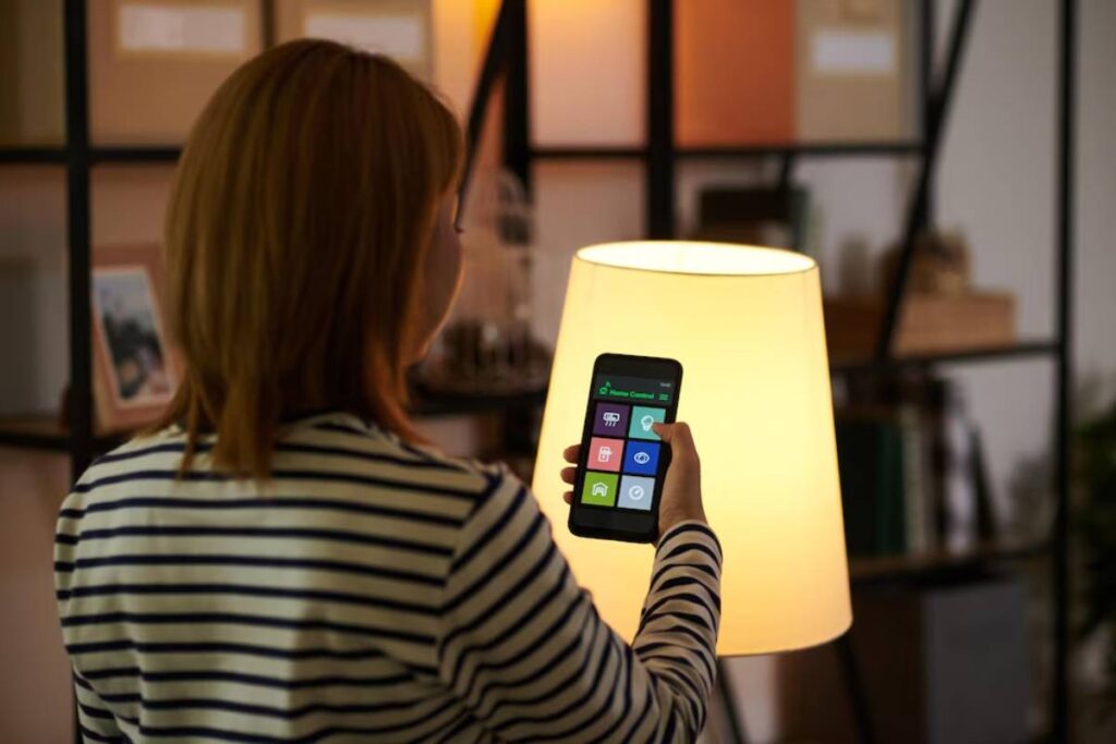 A woman in striped shirt controls a smart lamp with her smartphone in a cozy, modern living space.