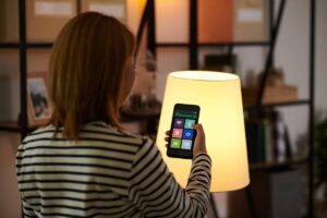 A woman in striped shirt controls a smart lamp with her smartphone in a cozy, modern living space.