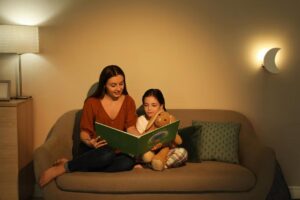 A cozy evening scene with a woman and a child sitting on a sofa, reading a storybook together, accompanied by a stuffed animal.
